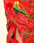Red dress with floral and parrot embroidery on a beige background.