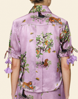 Person wearing a purple floral shirt and shorts on a light background shot from the back