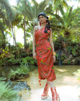 Woman in a red dress standing in a tropical setting with palm trees and water.