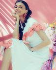 Woman in a white shirt and cape with floral applique on pink background