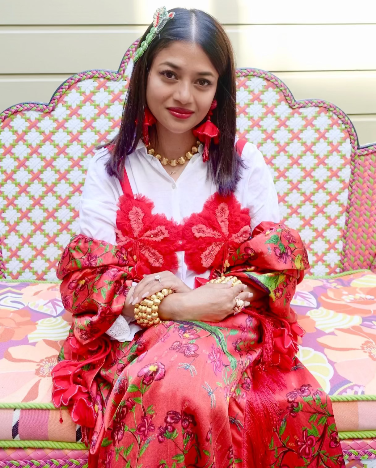Woman in red embroidered top over white shirt sitting on a colorful couch.