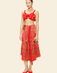 Woman wearing a red floral skirt and bra top outfit on a beige background