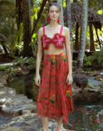 Woman in a red outfit standing in a tropical setting with palm trees and a pond.