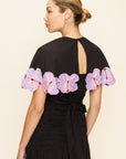 Woman wearing a black cape with pink floral appliqué seen from the back