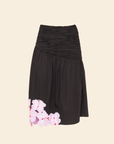 A midi skirt with floral applique on the lower right side, predominantly black in color.