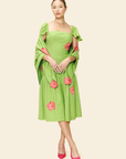 Woman wearing a green dress amd a shawl with pink floral patterns on a plain background