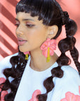 Woman with braided hair wearing pink floral earrings against a pink background