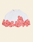 White top with coral pink floral trim on a beige background
