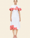 Woman wearing a white cape with pink floral appliqué and a white skirt on a beige background