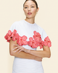Woman wearing a white cape with pink floral appliqué and a white skirt on a beige background