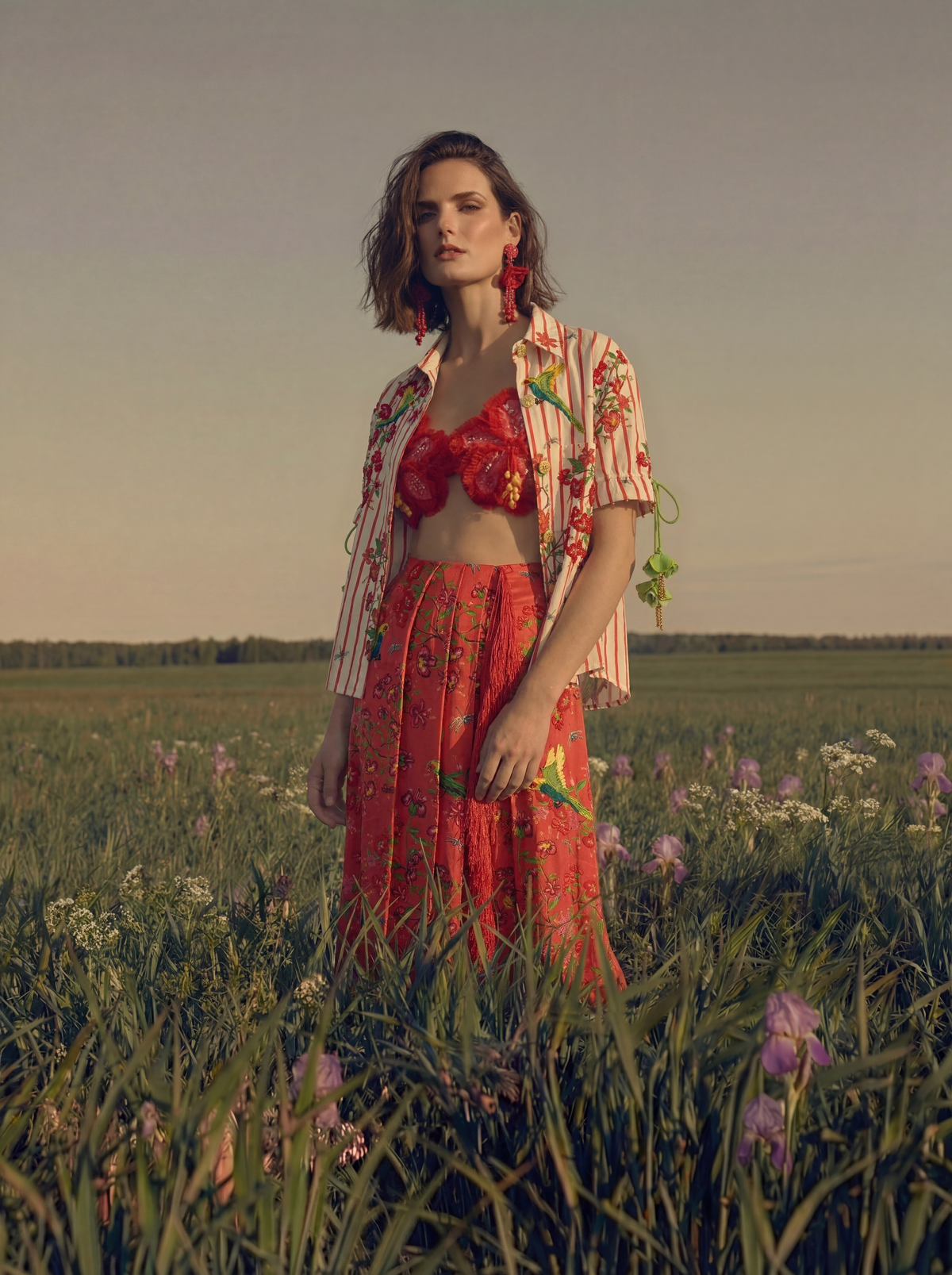 Woman in a red outfit standing in a field with a sunset background