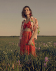 Woman in a red outfit standing in a field with a sunset background