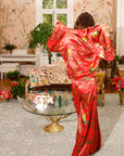Person wearing a red floral outfit in a decorated room with floral wallpaper and furniture.