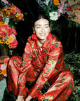 Woman in red floral outfit sitting on the floor surrounded by flowers and foliage
