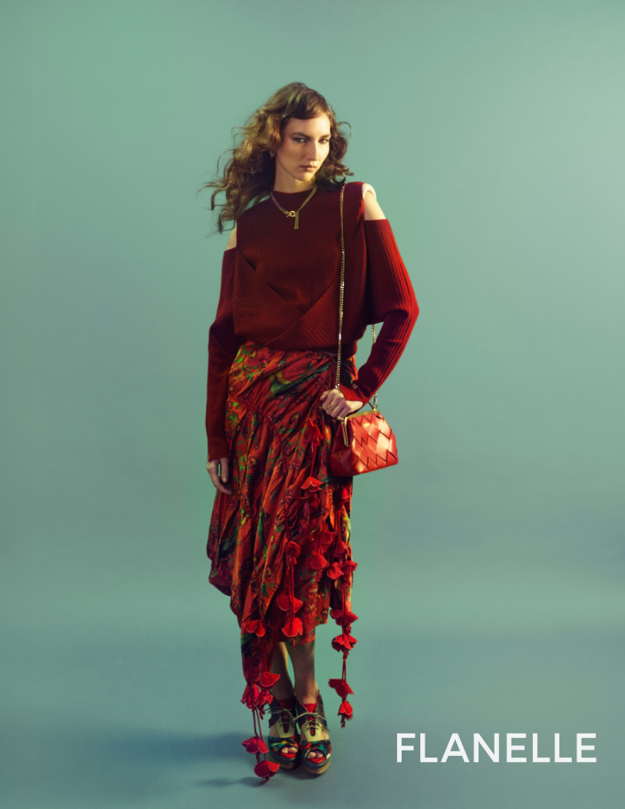 Woman wearing a red outfit with floral details and a matching bag on a light green background.