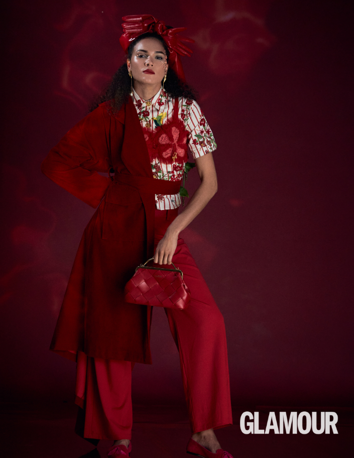 Woman in a red outfit with a floral top against a red background, holding a red handbag.