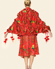 Woman wearing red floral skirt with fringe, red floral bra top and floral scarf with tassels and green parakeet print shown from the back