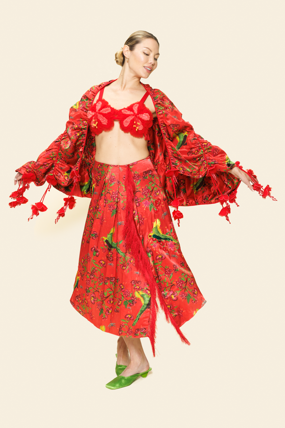 Woman wearing red floral skirt with fringe, red floral bra top and floral scarf with tassels and green parakeet print