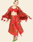 Woman wearing red floral skirt with fringe, red floral bra top and floral scarf with tassels and green parakeet print