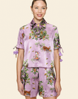 Person wearing a purple floral shirt and shorts on a light background