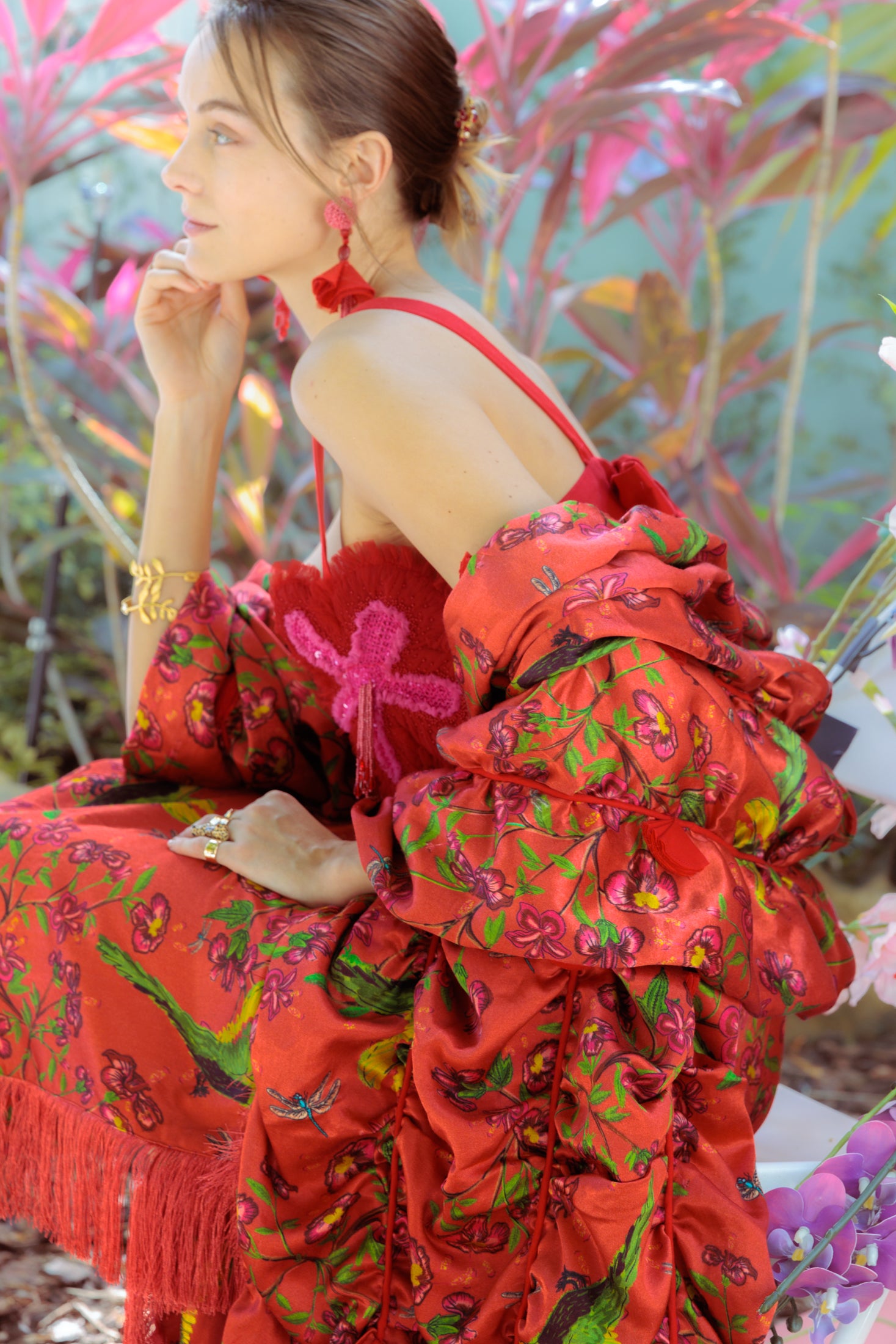 Woman in a red floral dress sitting among plants