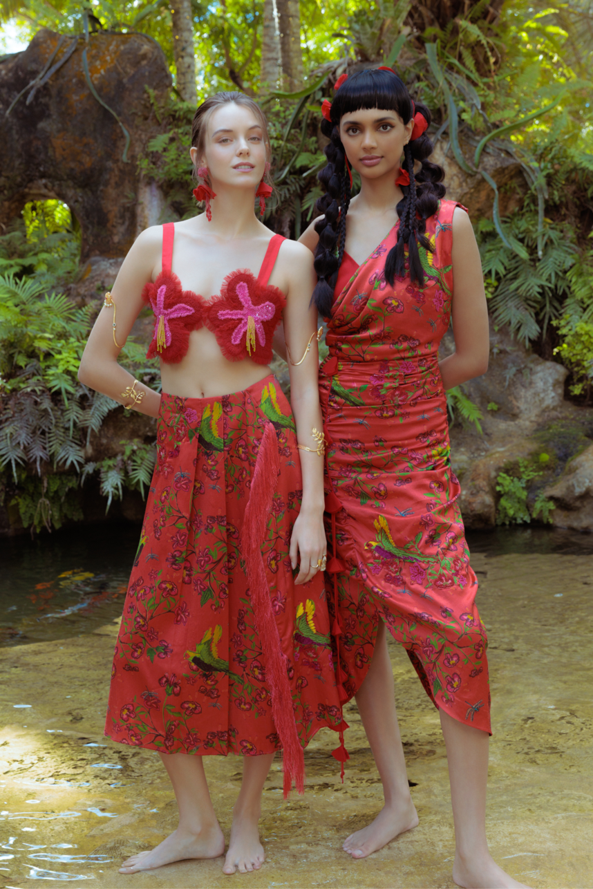 Two women in red outfits standing in a natural setting with greenery.