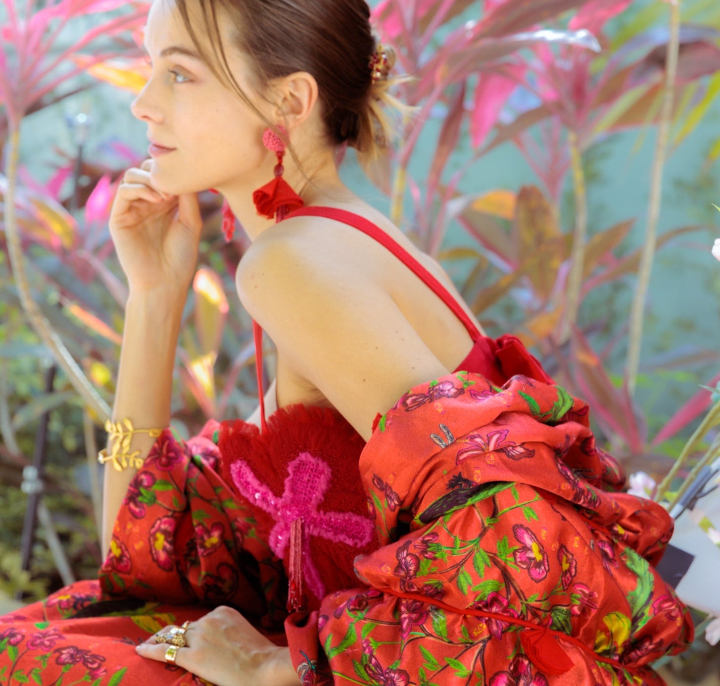Woman in a red floral dress and scarf sitting outdoors with plants in the background