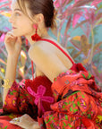 Woman in a red floral dress and scarf sitting outdoors with plants in the background