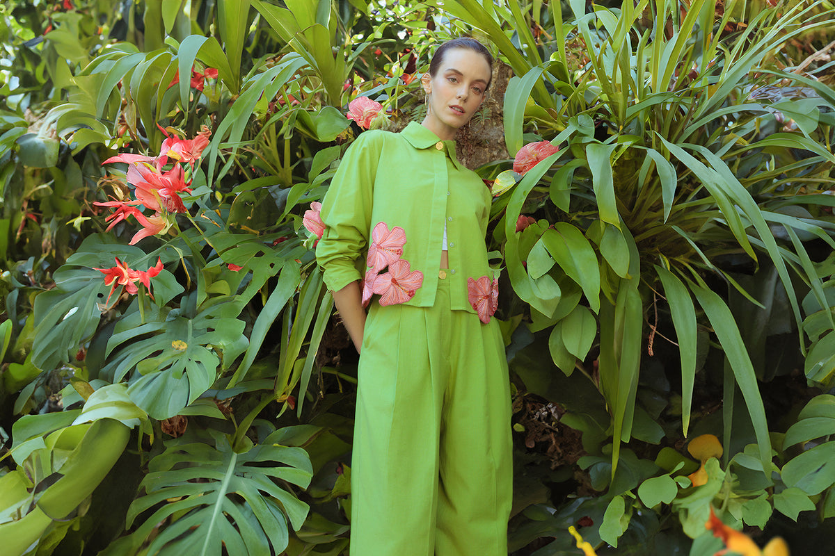 Person wearing a green outfit with pink floral appliqué, standing in a lush green garden.