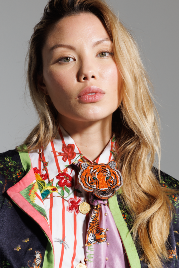 Woman wearing a colorful outfit with a prominent tiger brooch in a studio setting