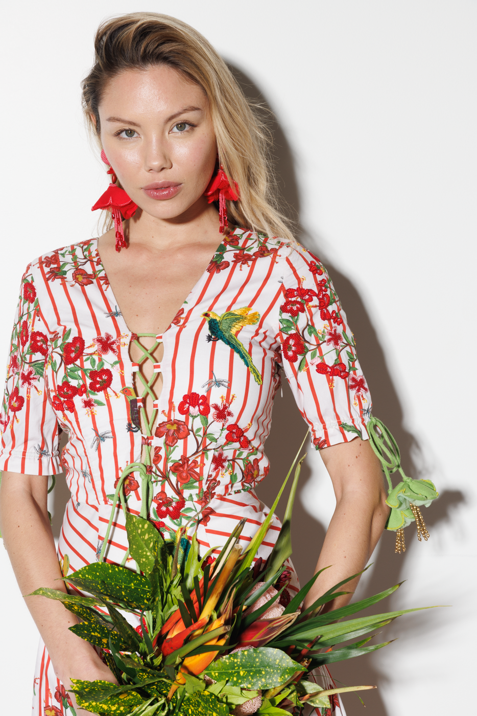 Woman in a red and white floral dress holding a bouquet of flowers against a white background