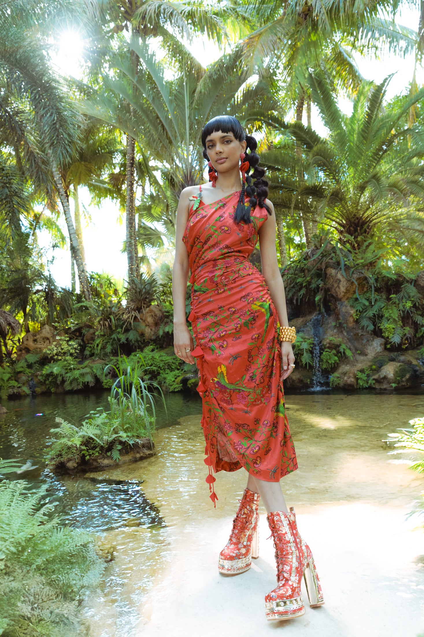 Woman in a red dress standing in a tropical setting with palm trees and water.