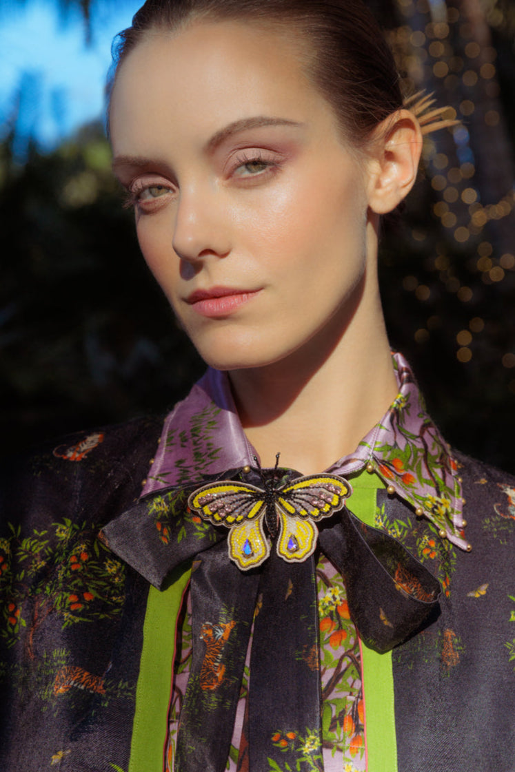 Woman wearing a colorful blouse and jacket with a butterfly accessory