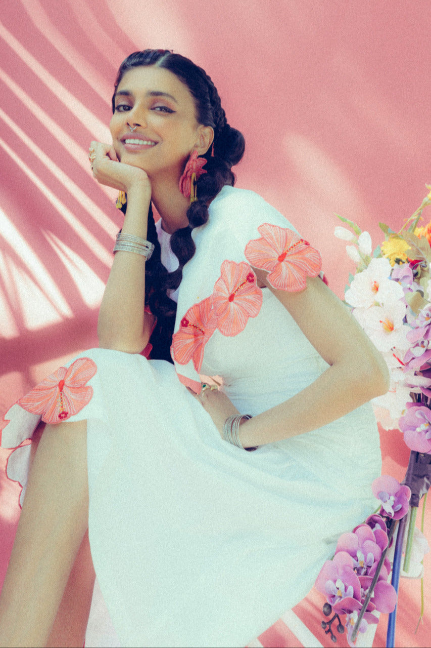 Woman in a white shirt and cape with floral applique on pink background