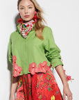 A woman wearing a green shirt with floral details and a red skirt with floral patterns on a white background