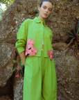 A woman wearing a bright green outfit with pink flowers against a natural  background
