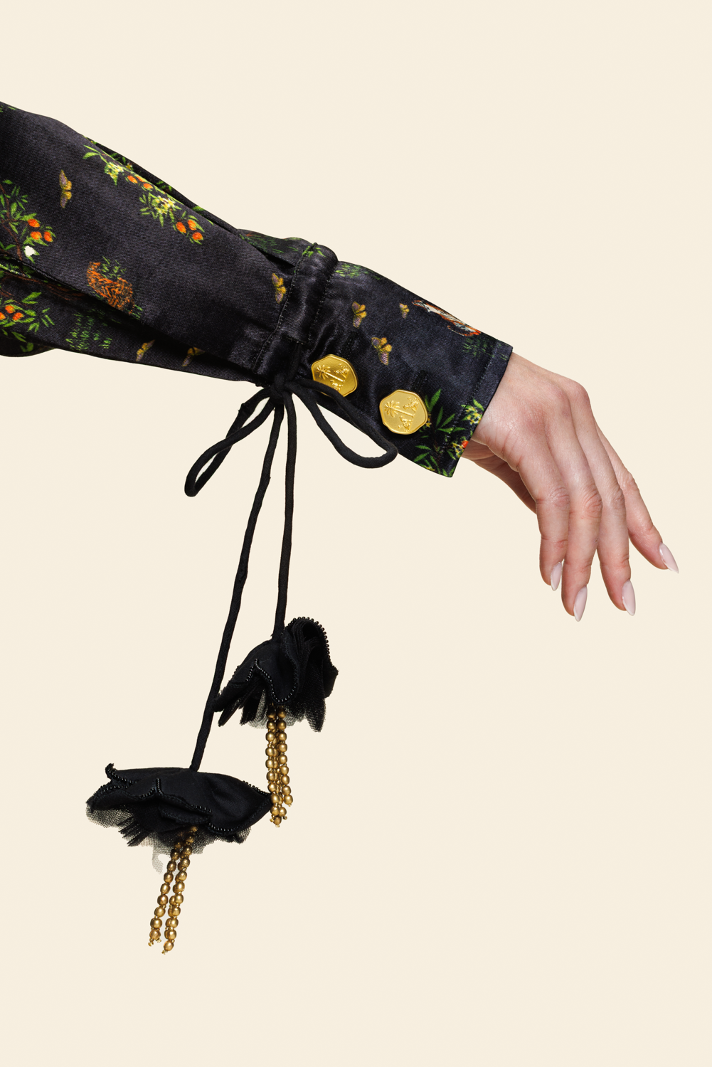 Close-up of a sleeve with gold beads and decorative florals on a string against beige background