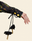 Close-up of a sleeve with gold beads and decorative florals on a string against beige background