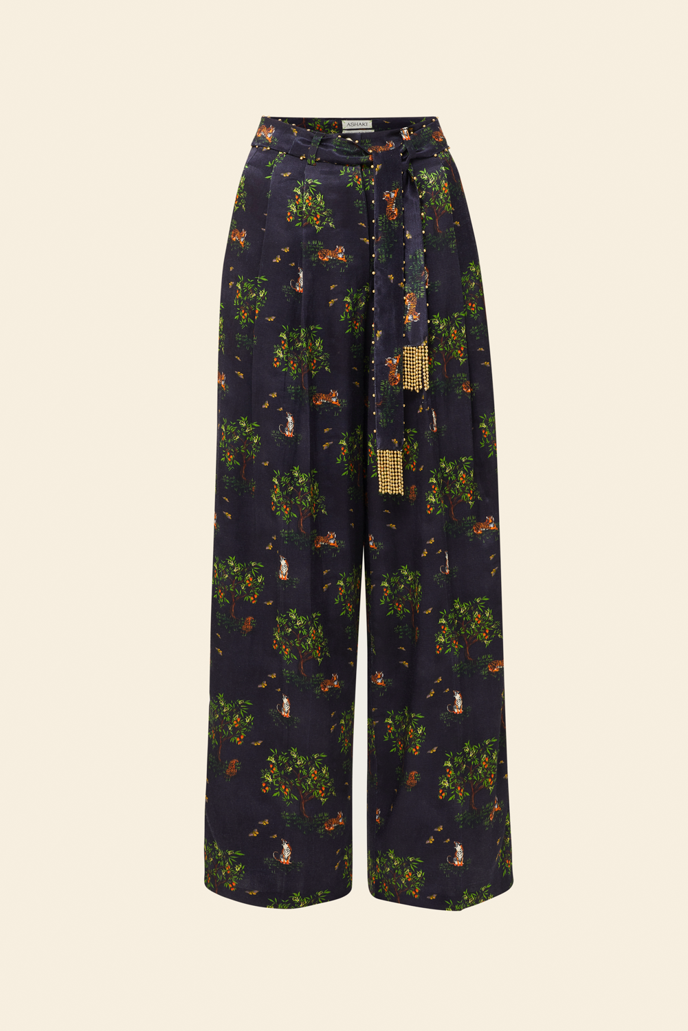 A pair of pleated trousers with a printed design featuring what appears to be a tropical landscape, paired with an embellished belt with fringe.