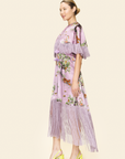 Woman wearing a purple floral dress with fringe details on a beige background