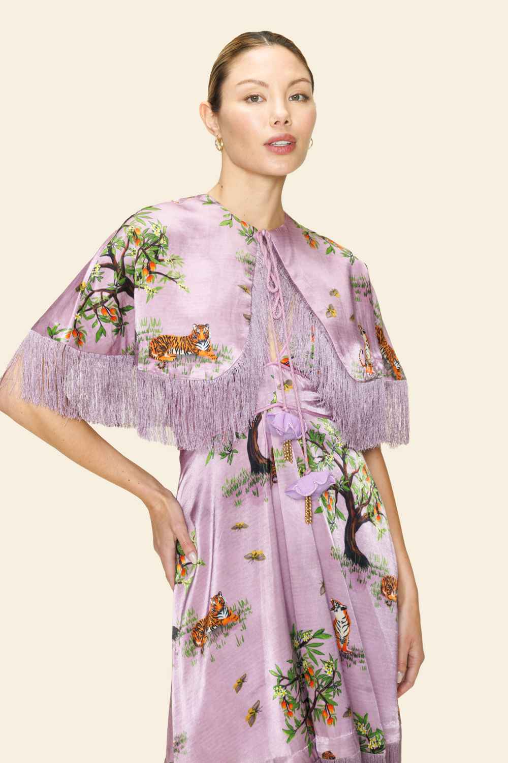 Woman wearing a floral and animal printed dress and a cape with fringes on a beige background