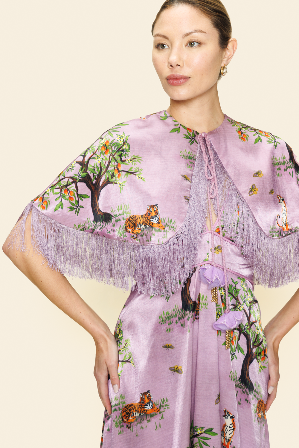Woman wearing a floral and animal printed dress and a cape with fringes on a beige background