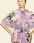Woman wearing a floral and animal printed dress and a cape with fringes on a beige background