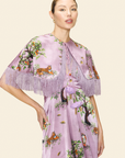 Woman wearing a floral and animal printed dress and a cape with fringes on a beige background