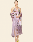 Woman wearing a floral and animal printed dress and a cape with fringes on a beige background