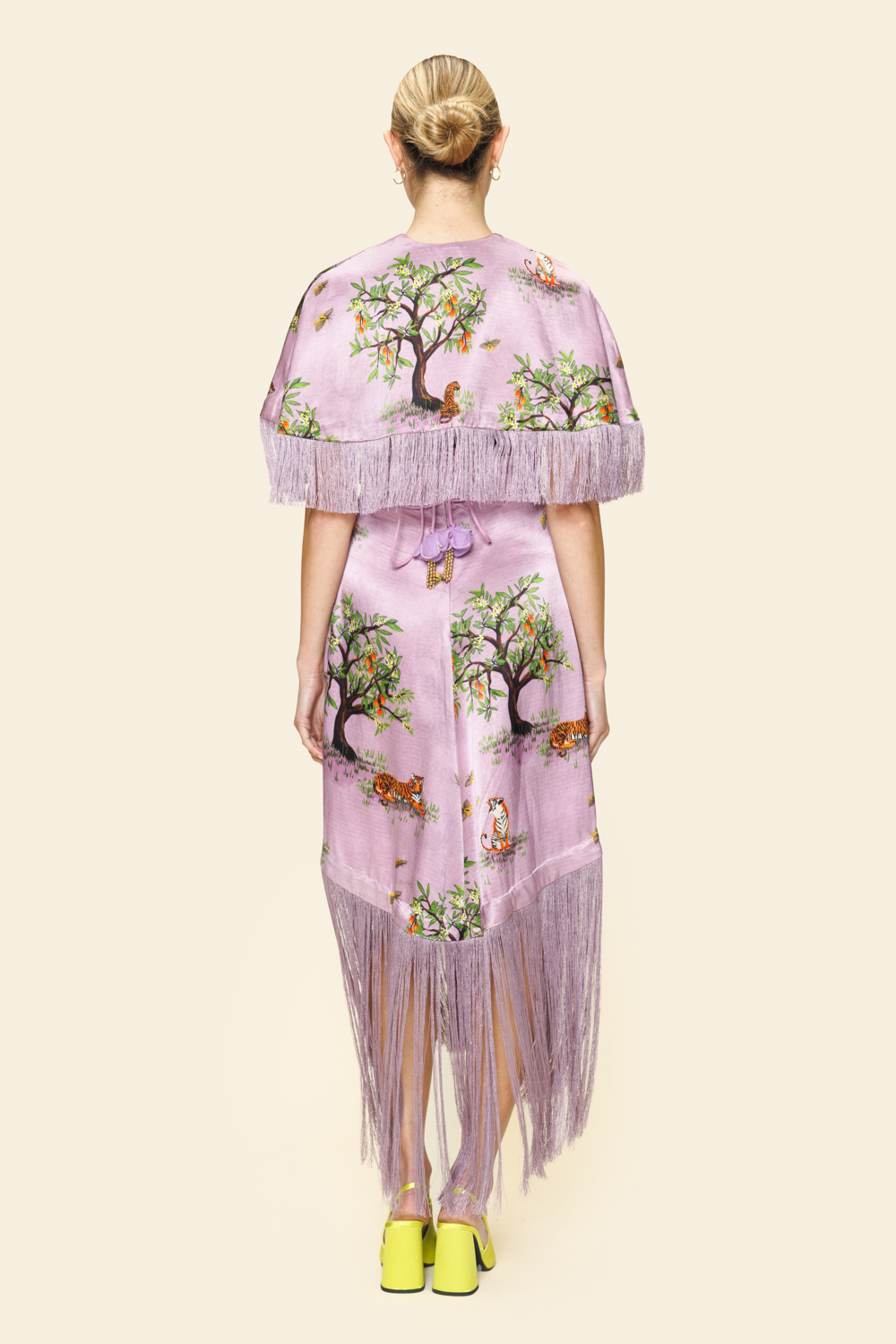 Woman wearing a floral and animal printed dress and a cape with fringes on a beige background
