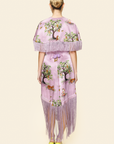 Woman wearing a floral and animal printed dress and a cape with fringes on a beige background