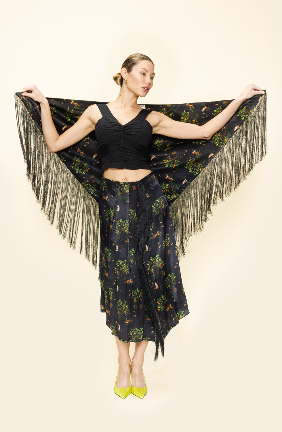 Woman wearing a black floral dress with fringe shawl on a plain background