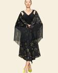 Woman wearing a black floral dress with fringe details on a plain background