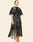 Woman wearing a dark floral dress with fringe details on a light background